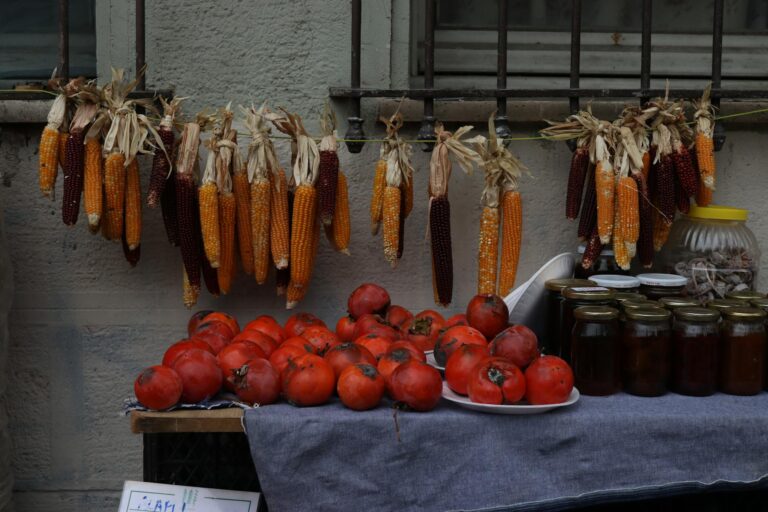 A vibrant market scene with hanging corn, fresh persimmons, and jarred preserves.