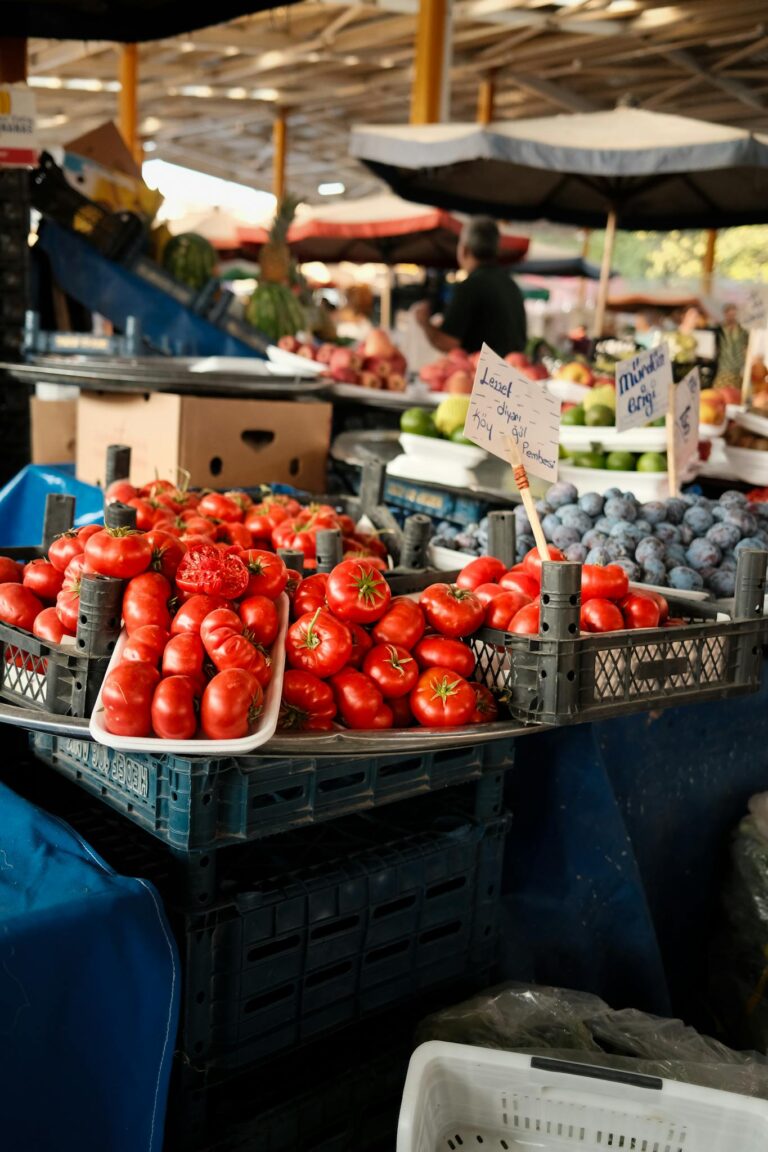 Colorful tomatoes and fruits at an outdoor farmers market, showcasing fresh local produce.